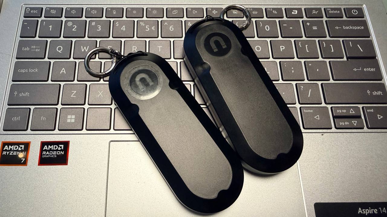 Two assembled black AirTag AA battery extender enclosures with keyrings attached